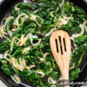 Cheesy Spinach Stuffed Chicken 11 Spinach and onions wilting in a skillet with a wooden spoon.