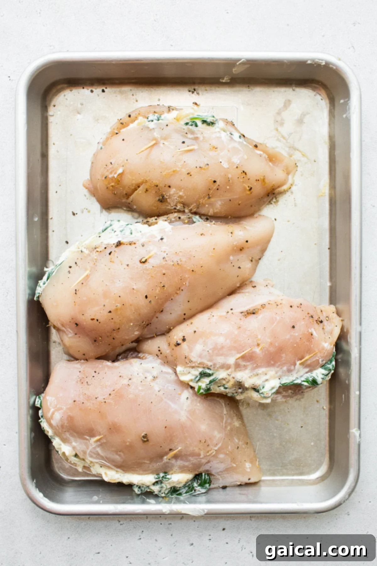Prepped Spinach Stuffed Chicken Breasts Stuffed chicken breast ready for baking on a baking sheet.