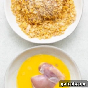 Chicken thighs being breaded with a cornflake mixture.