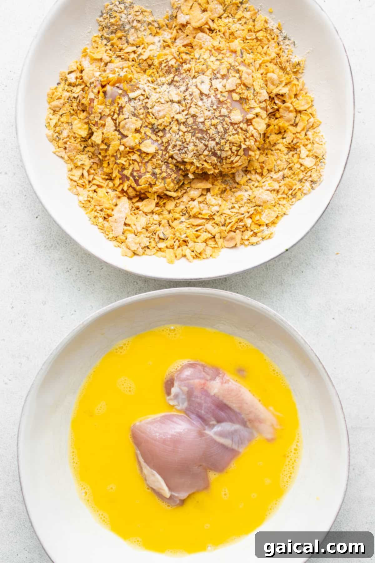 Chicken thighs being coated with the seasoned cornflake mixture in a mixing bowl.
