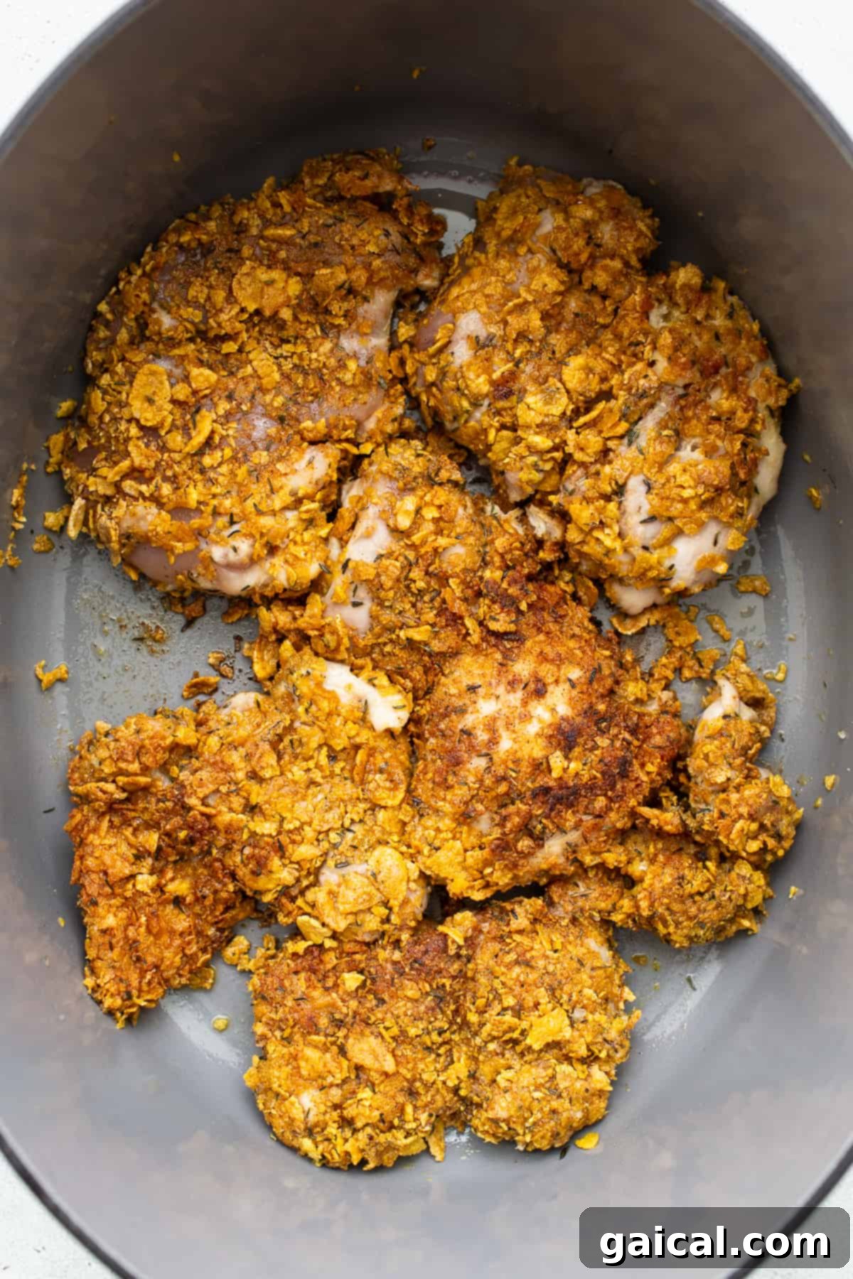 Crispy cornflake-crusted chicken thighs searing in a hot skillet with olive oil.