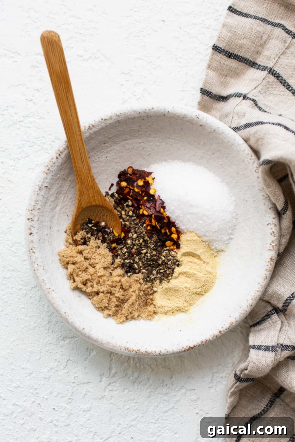 Make your own homemade steak seasoning with just 5 ingredients you likely already have in your spice cupboard, and you’ll be on your way to the most flavorful steak in no time. A bowl holds a savory steak seasoning mix of brown sugar, black pepper, crushed red pepper flakes, salt, and garlic powder, with a wooden spoon resting on the side.