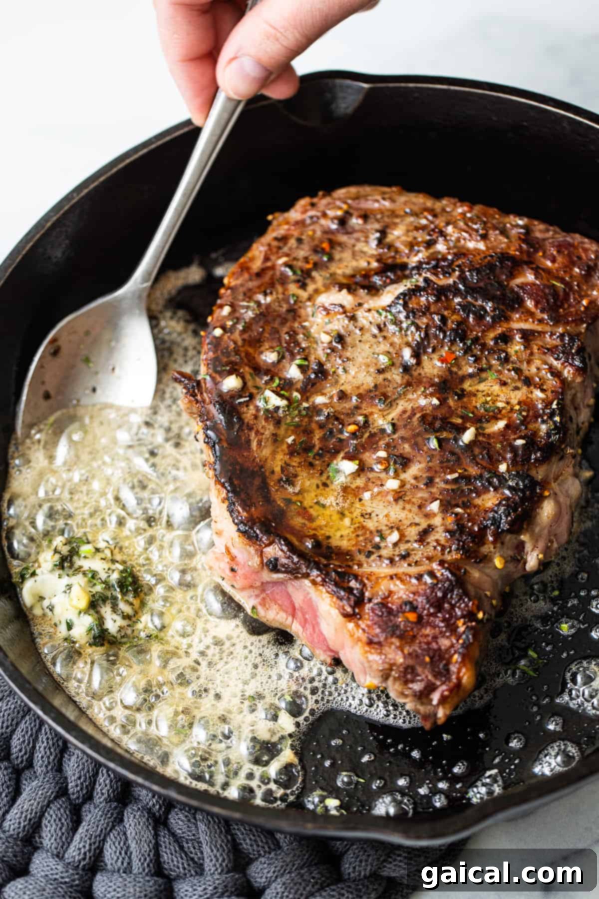 Cast Iron Steak Perfection 4 A spoon basting a sizzling steak with melted butter and herbs.