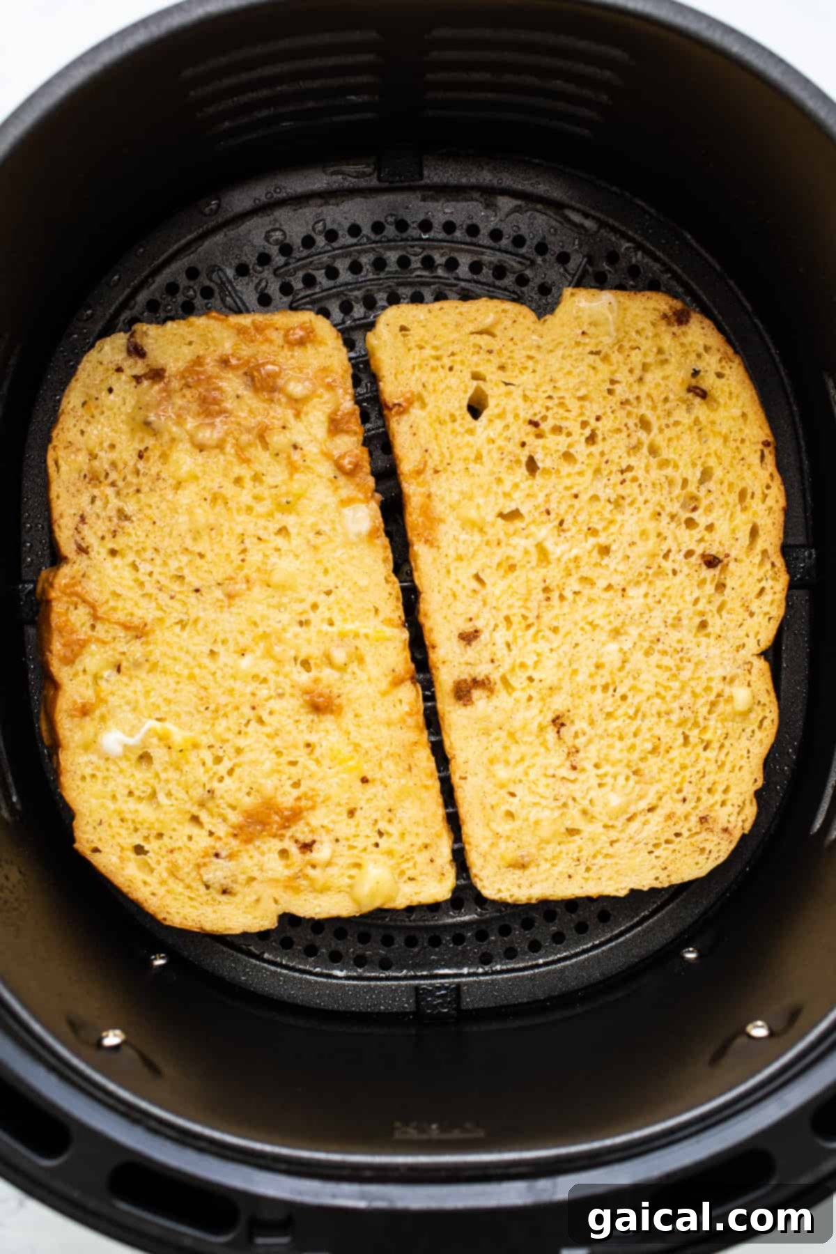 Two slices of golden-brown air fryer chunky monkey French toast cooking in an air fryer basket, with the top side perfectly browned.