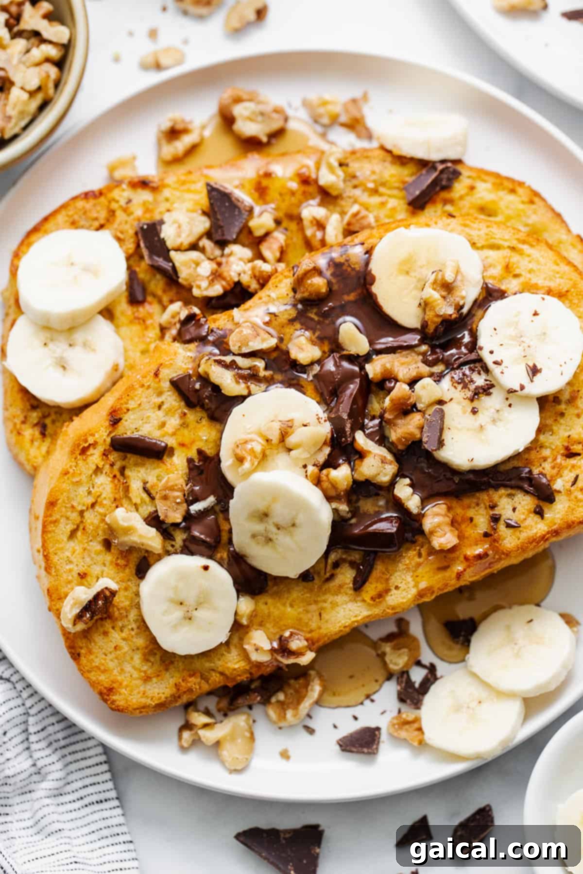 A beautifully plated Air Fryer Chunky Monkey French Toast, garnished with melted chocolate, crunchy roasted walnuts, and fresh banana slices, served on a white plate.