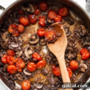 Mushrooms and tomatoes in a pan with a wooden spoon.