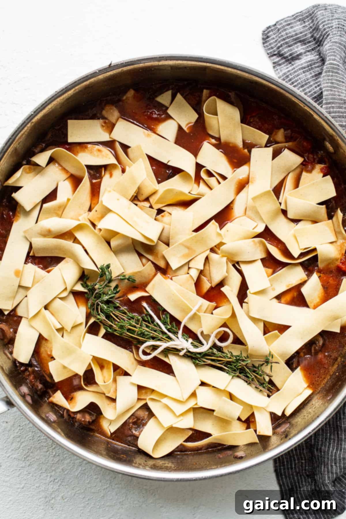 Pappardelle pasta submerged in savory sauce for a true one-pot experience. Pappardelle pasta delicately laid over a rich tomato sauce in a skillet, ready for cooking.