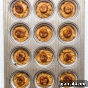 Muffin batter scooped into a muffin tin with banana slices on top
