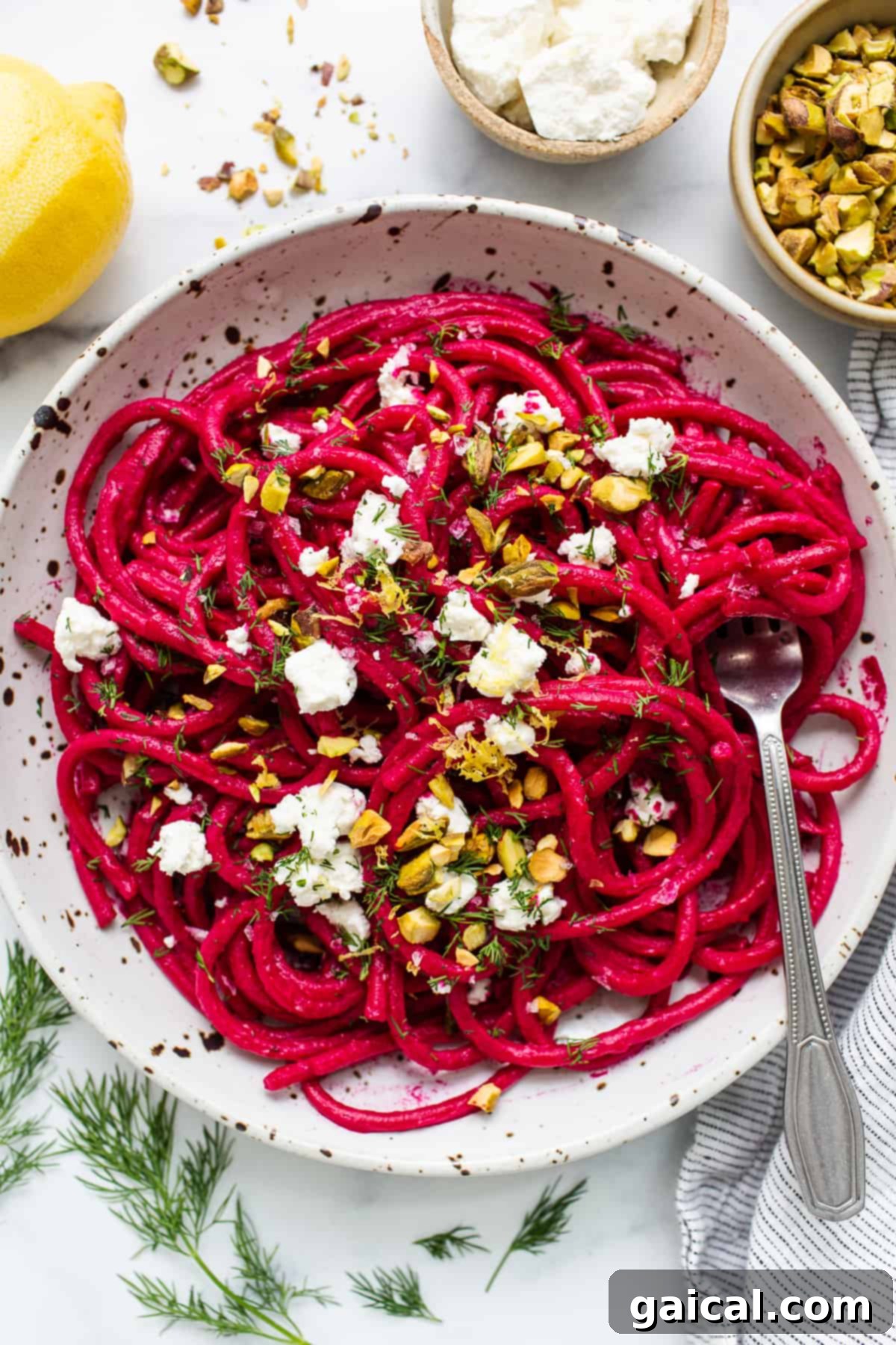 A bowl of vibrant pink roasted beet pasta, garnished with fresh herbs and crumbled goat cheese.