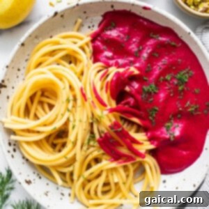 Cooked spaghetti tossed with creamy beet sauce on a white plate, ready for garnishing.