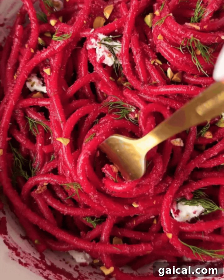 A beautifully presented serving of pink beet pasta, topped with fresh herbs and crumbled goat cheese.