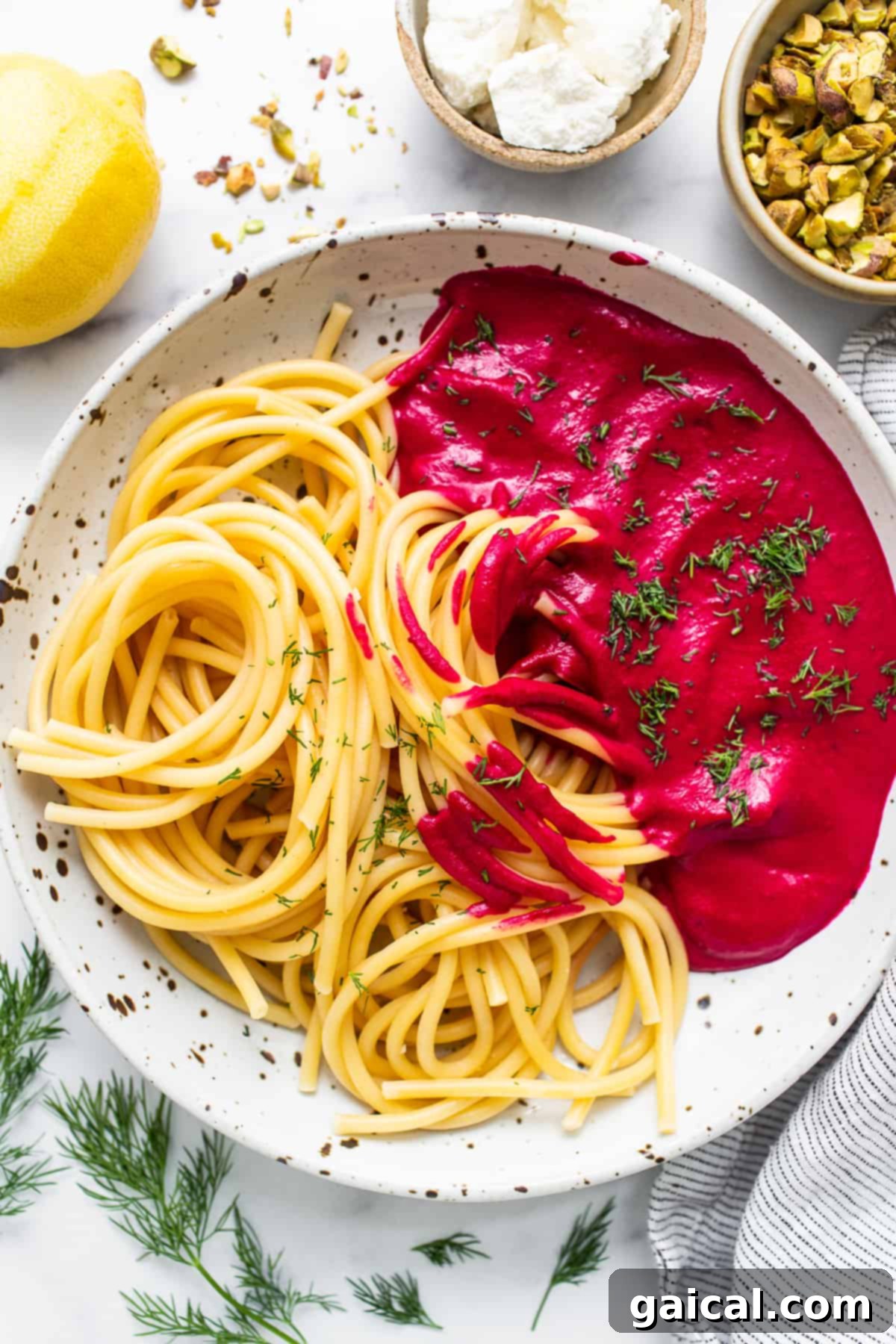 A close-up of a bowl of roasted beet pasta, beautifully garnished with crumbled goat cheese, fresh dill, and crushed pistachios.