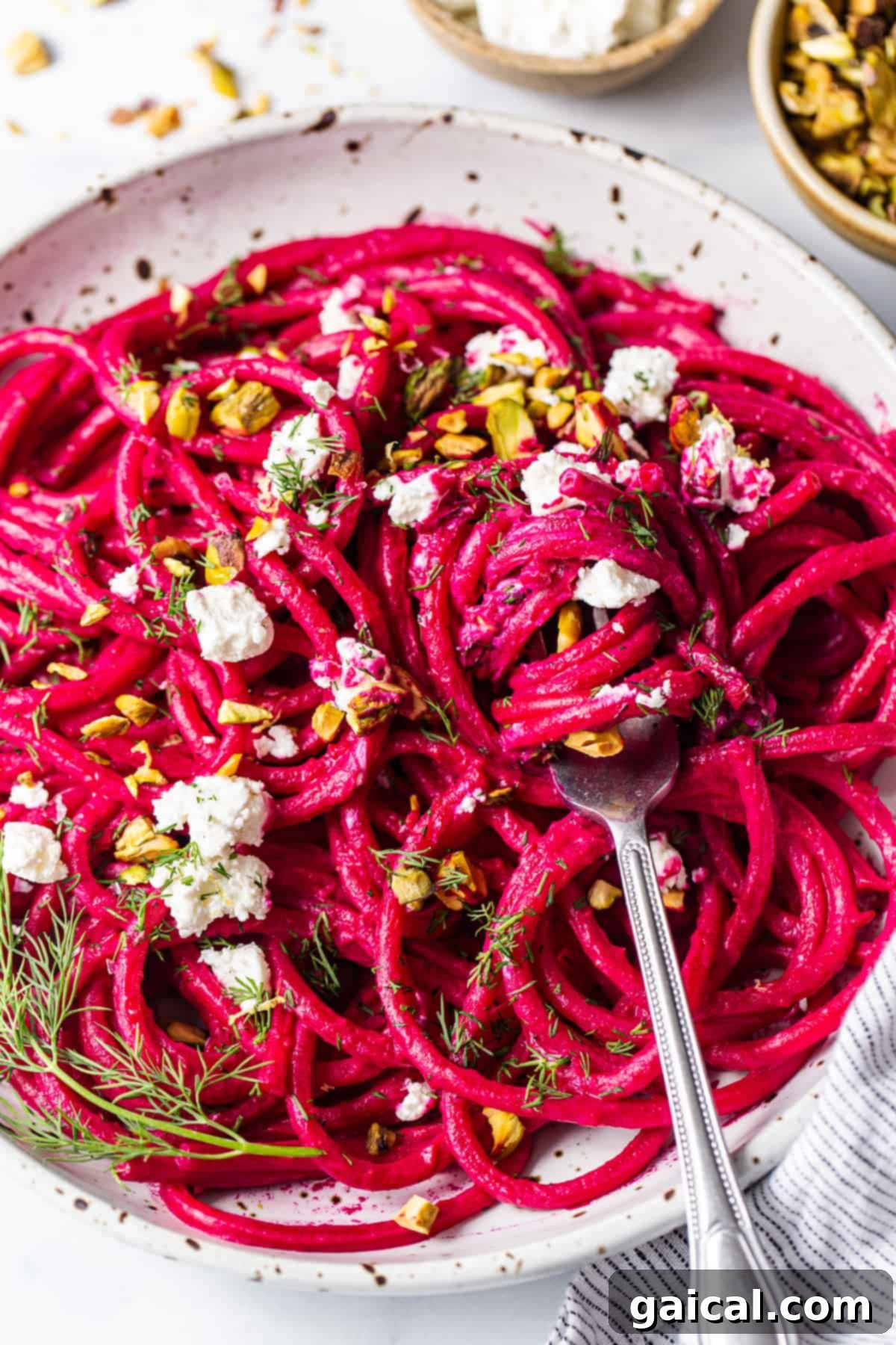 A beautifully arranged bowl of roasted beet pasta, topped with generous crumbles of goat cheese, pistachios, and fresh dill.