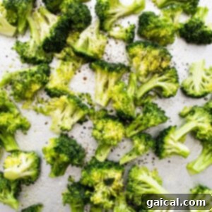Broccoli florets seasoned with salt and pepper, spread on a baking sheet, ready for the oven.