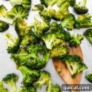 A serving of roasted broccoli on a white plate with a wooden spoon, showcasing its readiness.