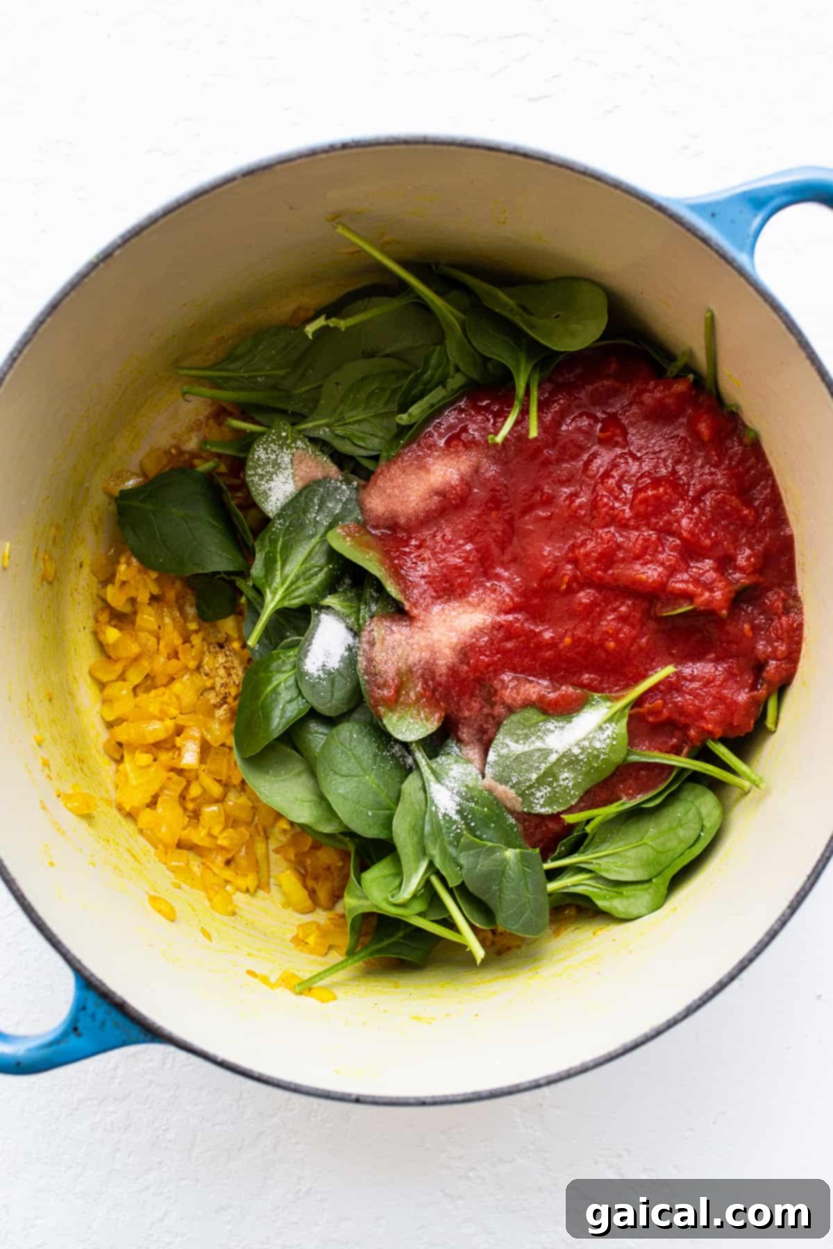 Sautéing Aromatics for a Rich Lentil Curry Base Fresh spinach, vibrant crushed tomatoes, and thinly sliced onions simmering in a Dutch oven, forming the aromatic base for the curry sauce.