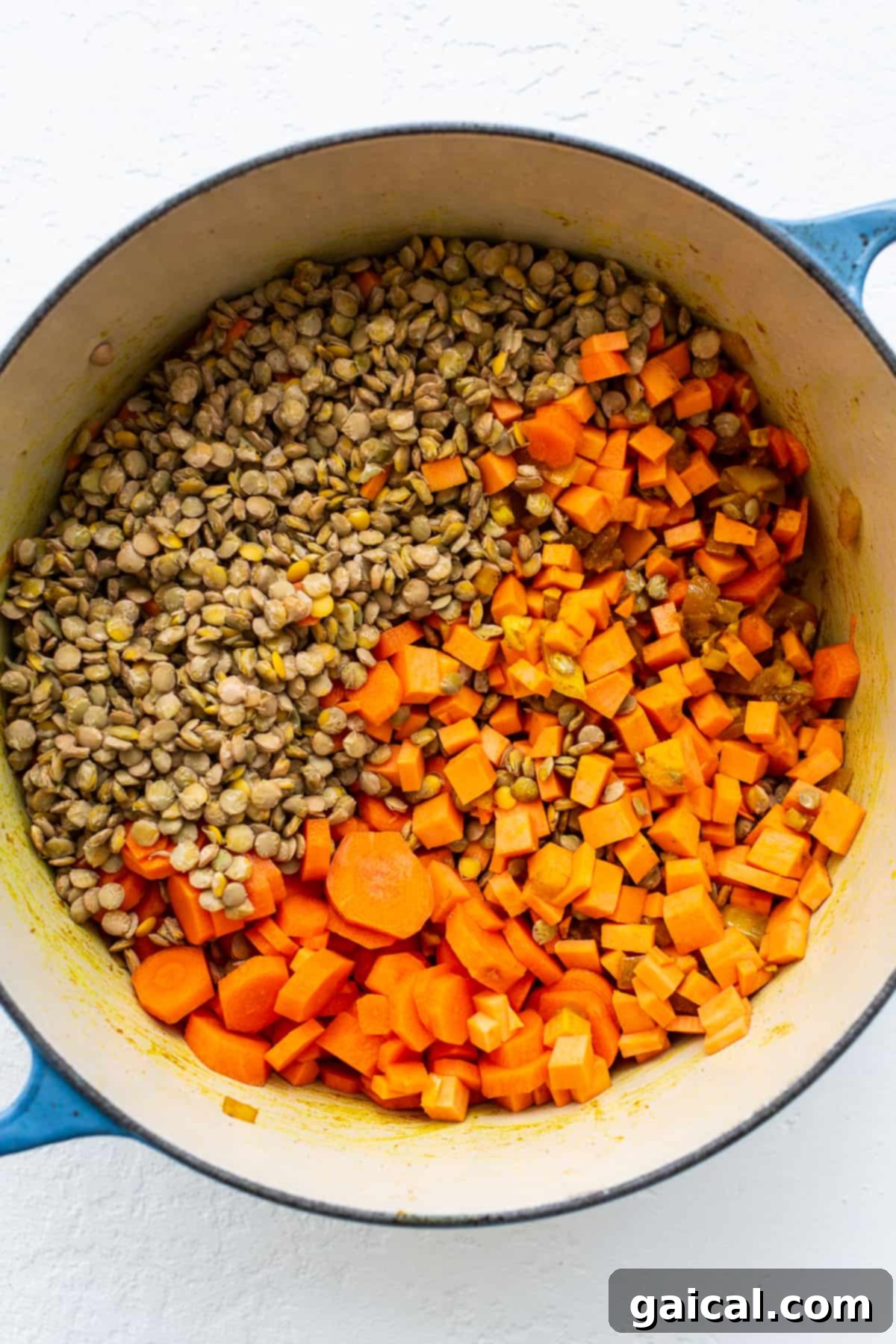 Prepping Vegetables and Lentils for a Rich Curry Base Cubed sweet potatoes and dry green lentils mixed with aromatic spices in a Dutch oven, ready for liquid to be added and simmered.