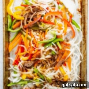 Sliced bell peppers and onions seasoned on a baking sheet.