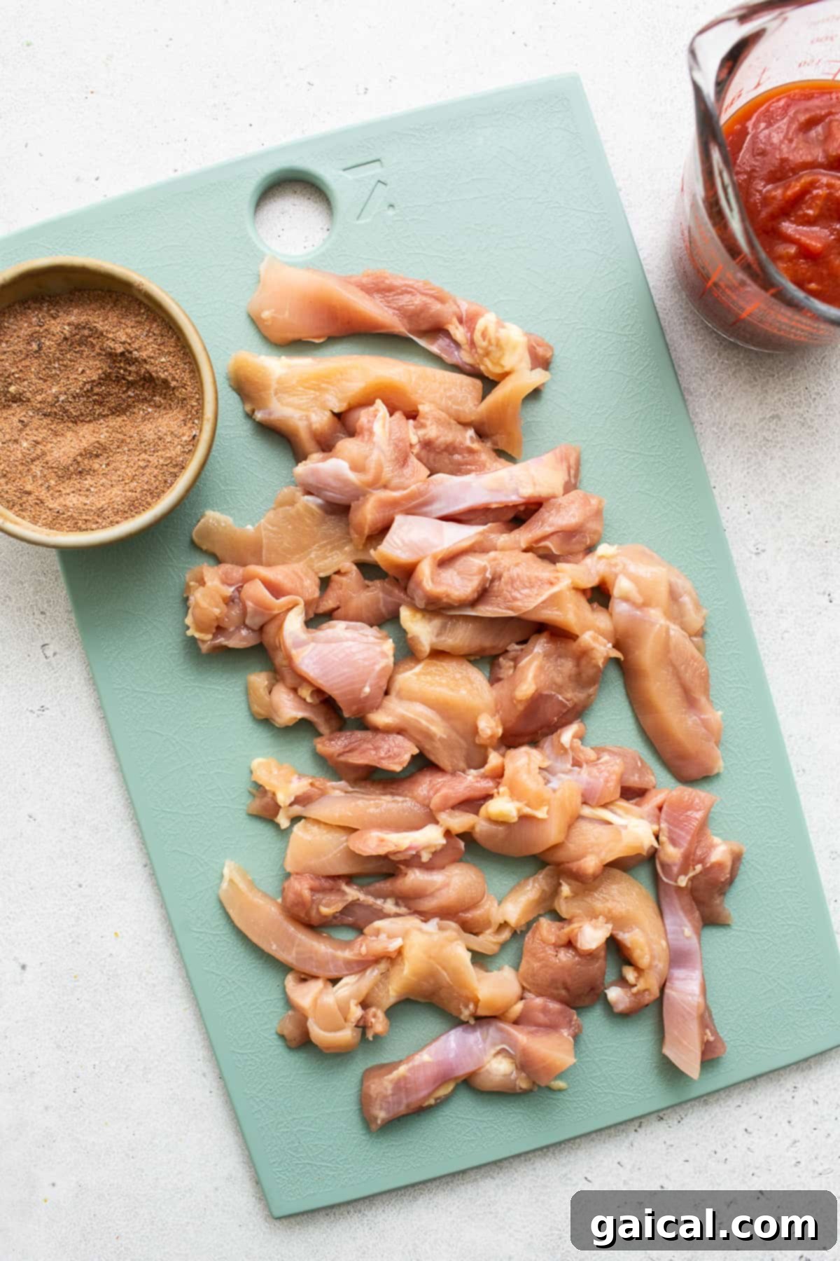 Raw boneless, skinless chicken thighs on a cutting board, ready for slicing.