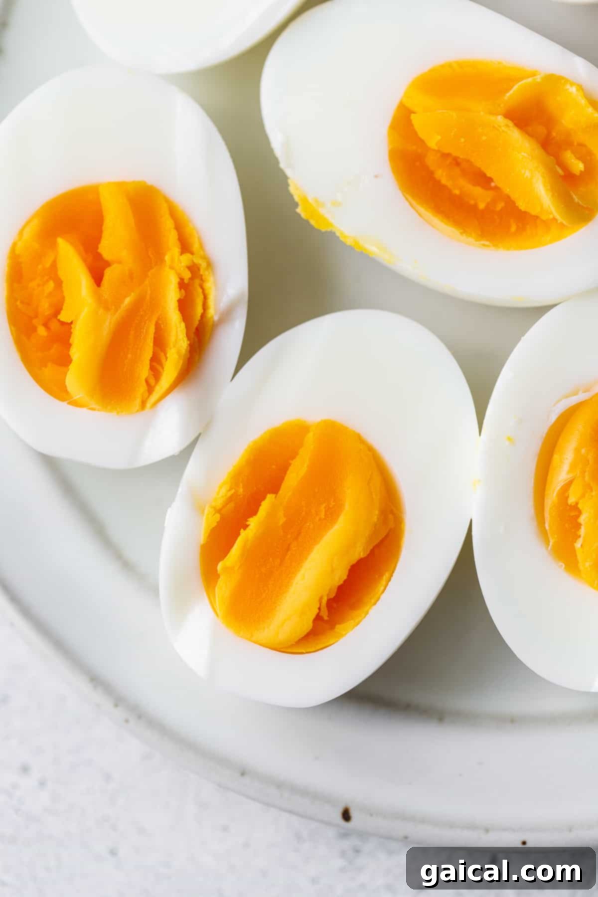 Sliced Air Fryer Hard Boiled Eggs with Perfect Yolks Two air-fried hard boiled eggs, expertly cut in half to reveal their perfectly cooked, bright yellow yolks, arranged artfully on a white plate.