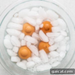 A glass bowl filled with ice water and cooked eggs, chilling to prepare them for easy peeling and to stop the cooking process.