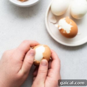 A person carefully peeling the shell from a freshly hard boiled egg, demonstrating the ease of the peeling process after the ice bath.