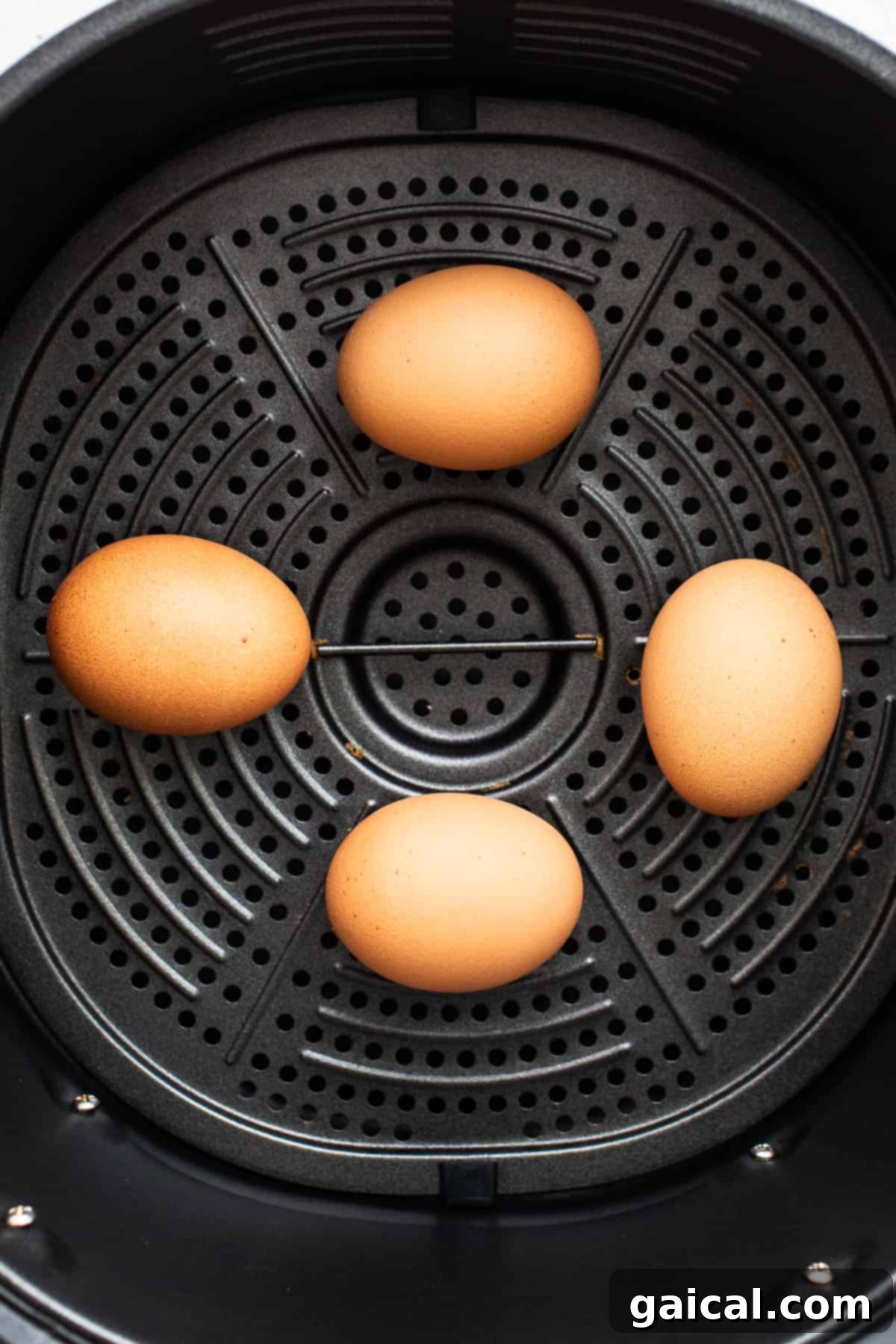 Eggs Placed Evenly in the Air Fryer Basket Four fresh, whole eggs carefully arranged in the basket of an air fryer, poised for a perfectly even cooking process.