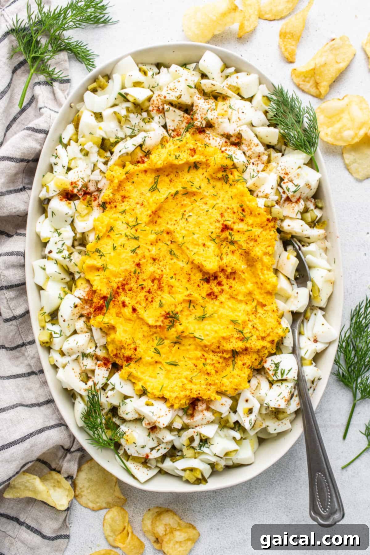 A beautifully presented serving bowl of creamy deviled egg salad, ready to be enjoyed. Deviled egg salad in a pristine white serving bowl, elegantly garnished with a sprinkle of paprika and a generous scattering of fresh dill.