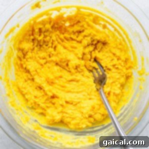 Devilishly Good Egg Spread 7 Creamy, mashed egg yolks mixed with condiments in a bowl, with a fork for blending.