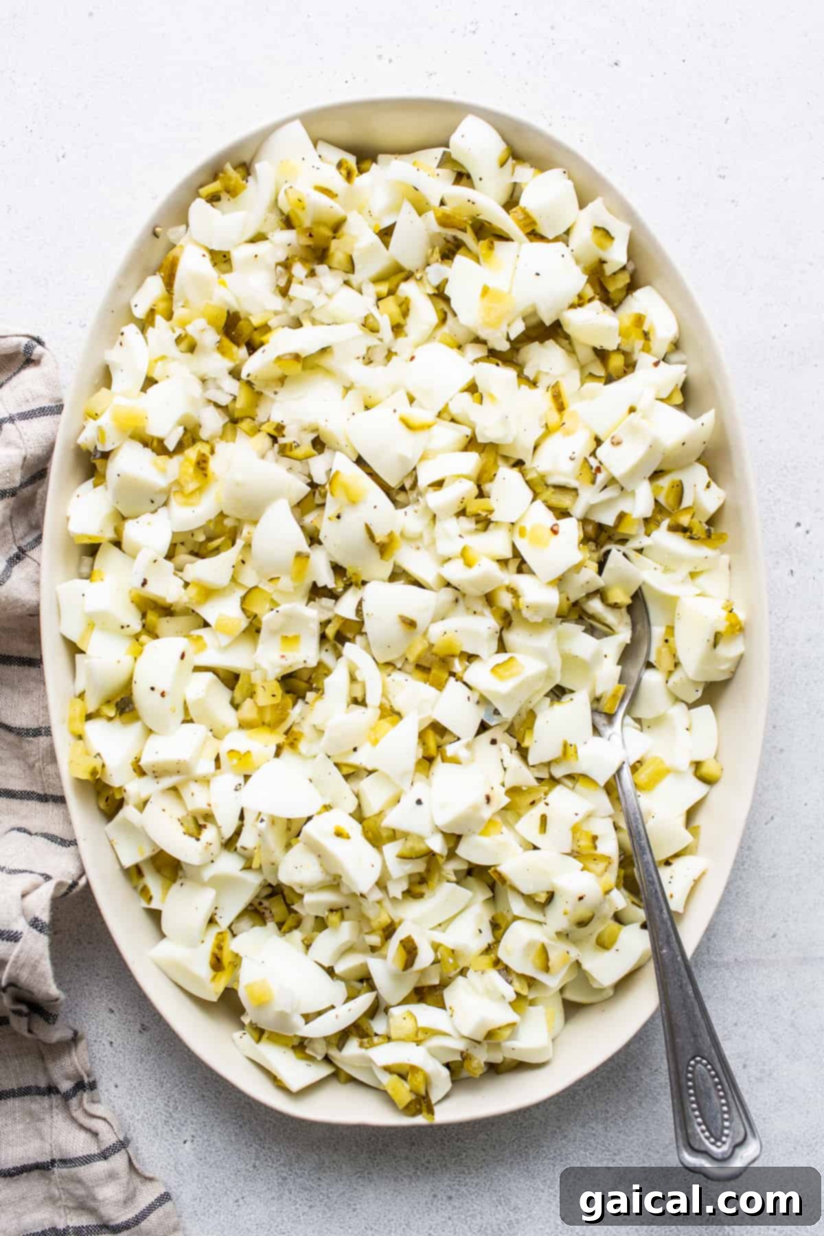 Seasoned chopped egg whites, a key component of the deviled egg salad. Roughly chopped egg whites, glistening from the vinegar-sugar mixture, displayed in a white bowl with a serving spoon nestled within.