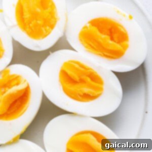 Devilishly Good Egg Spread 3 Several perfectly cooked hard-boiled eggs with their shells cracked, resting on a white plate, ready for easy peeling.