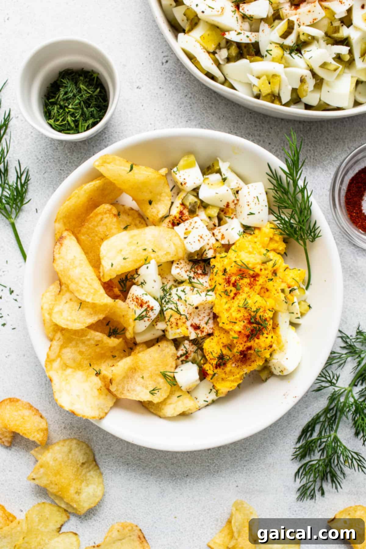 Deviled egg salad presented with potato chips for a delightful dipping experience. A generous bowl of deviled egg salad, impeccably garnished and accompanied by a large pile of crispy golden potato chips, perfect for dipping.