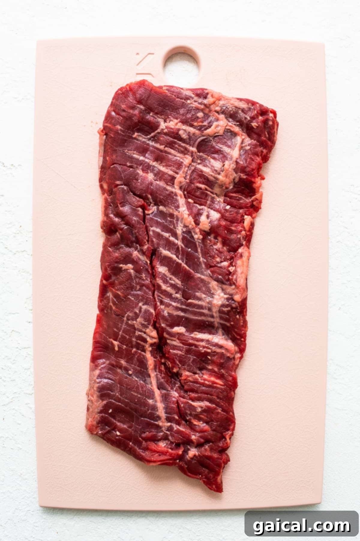 Mastering Skirt Steak Cooking 3 Raw skirt steak, seasoned and ready for marination, displayed on a wooden cutting board.