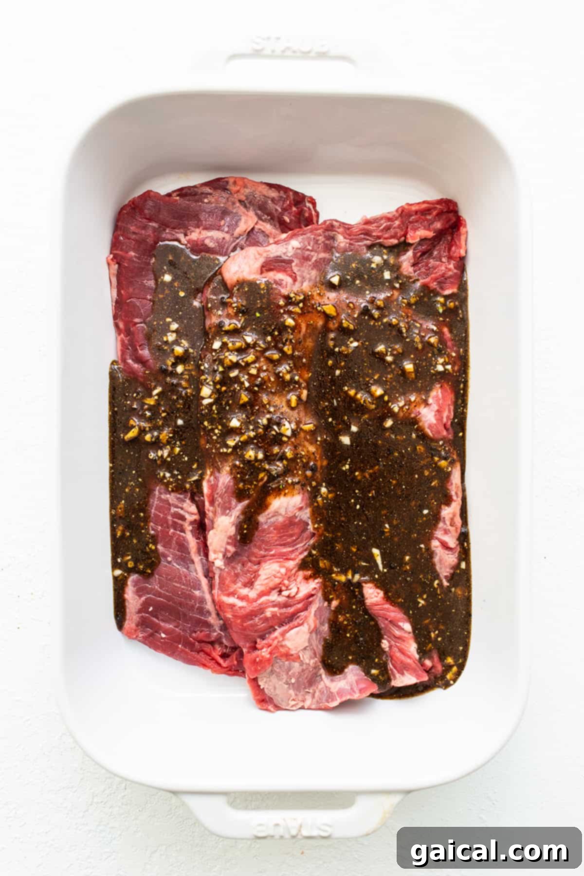 Mastering Skirt Steak Cooking 4 Raw skirt steak in a baking dish, generously topped with a rich, dark marinade, ready to be refrigerated.