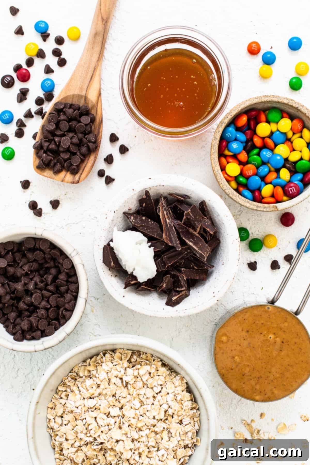 Bowls filled with the distinct ingredients for monster cookie oat cups: quick oats, creamy peanut butter, melted chocolate, and colorful M&M's.