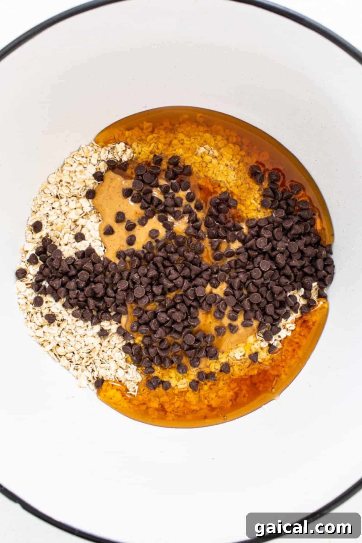 All the dry ingredients for monster cookie oat cups, including quick oats and mini chocolate chips, are shown mixed in a bowl.
