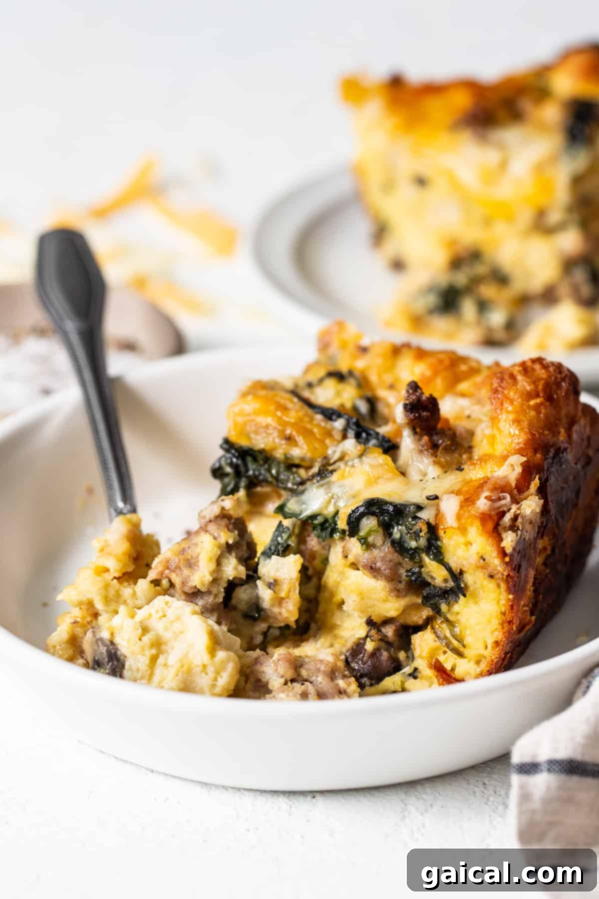 Fluffy, Custardy Classic Breakfast Strata Slice of breakfast strata on a plate with a fork, showing its fluffy, custardy layers.
