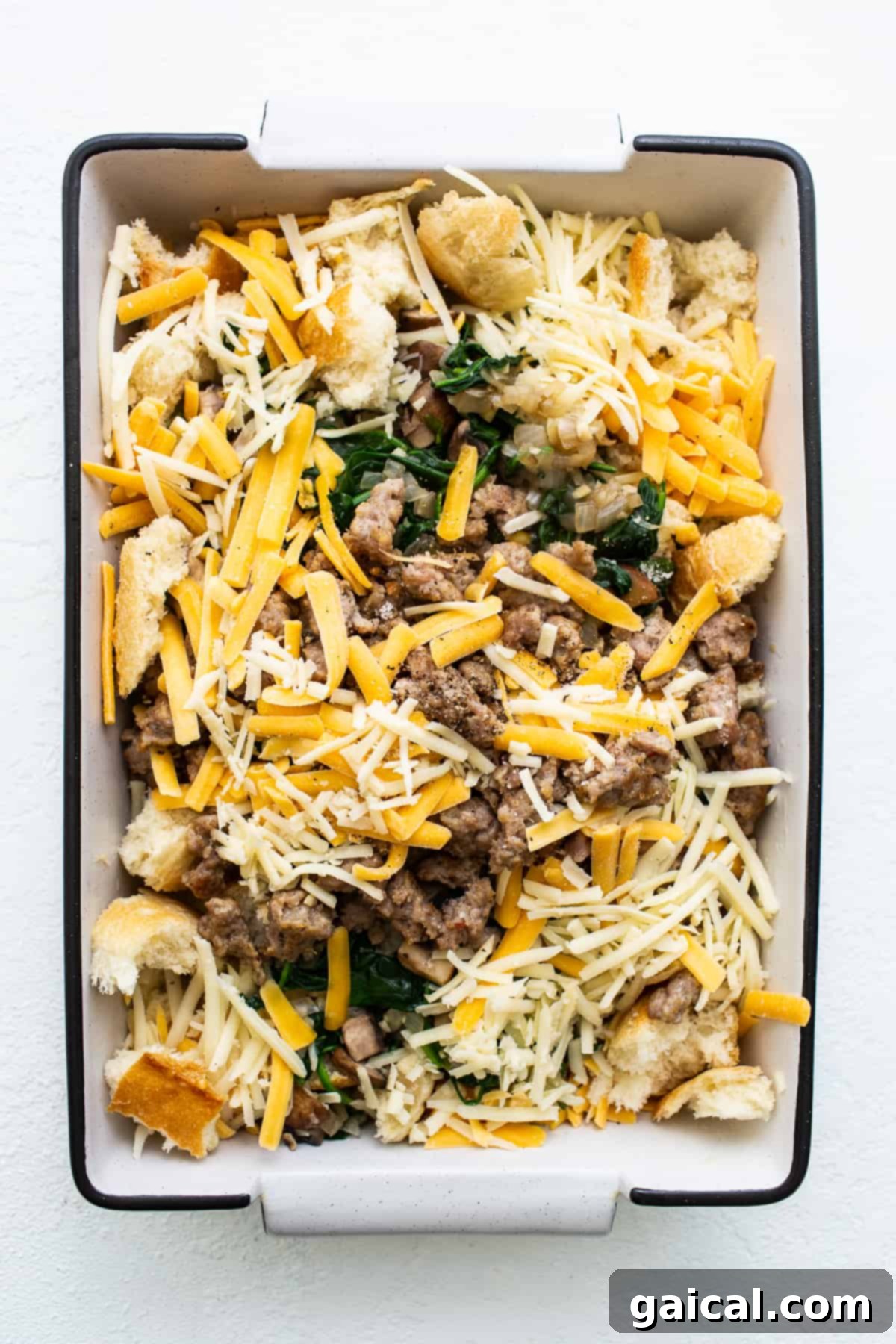 Assembled Strata Ready for Soak Unbaked breakfast strata ingredients meticulously arranged in a casserole dish, showcasing layers of bread, sausage, veggies, and cheese before the custard is poured over.