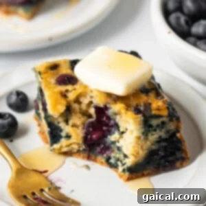 Golden Blueberry Coffee Cake 7 A delicious slice of blueberry breakfast cake on a plate, ready to be eaten, with a fork beside it.
