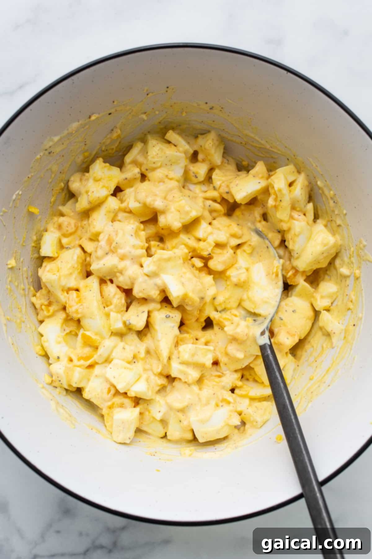 Classic egg salad is made with perfectly cooked hard-boiled eggs and a yummy sauce. A generous bowl of classic egg salad, beautifully garnished and ready to be served, highlighting its rich and creamy texture.