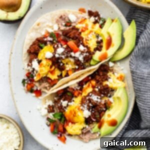 Two fully assembled breakfast tacos on a white plate with a fork, garnished with fresh cilantro.