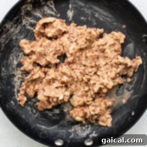Morning Taco Delights 4 Refried beans being mashed in a pan with a fork.