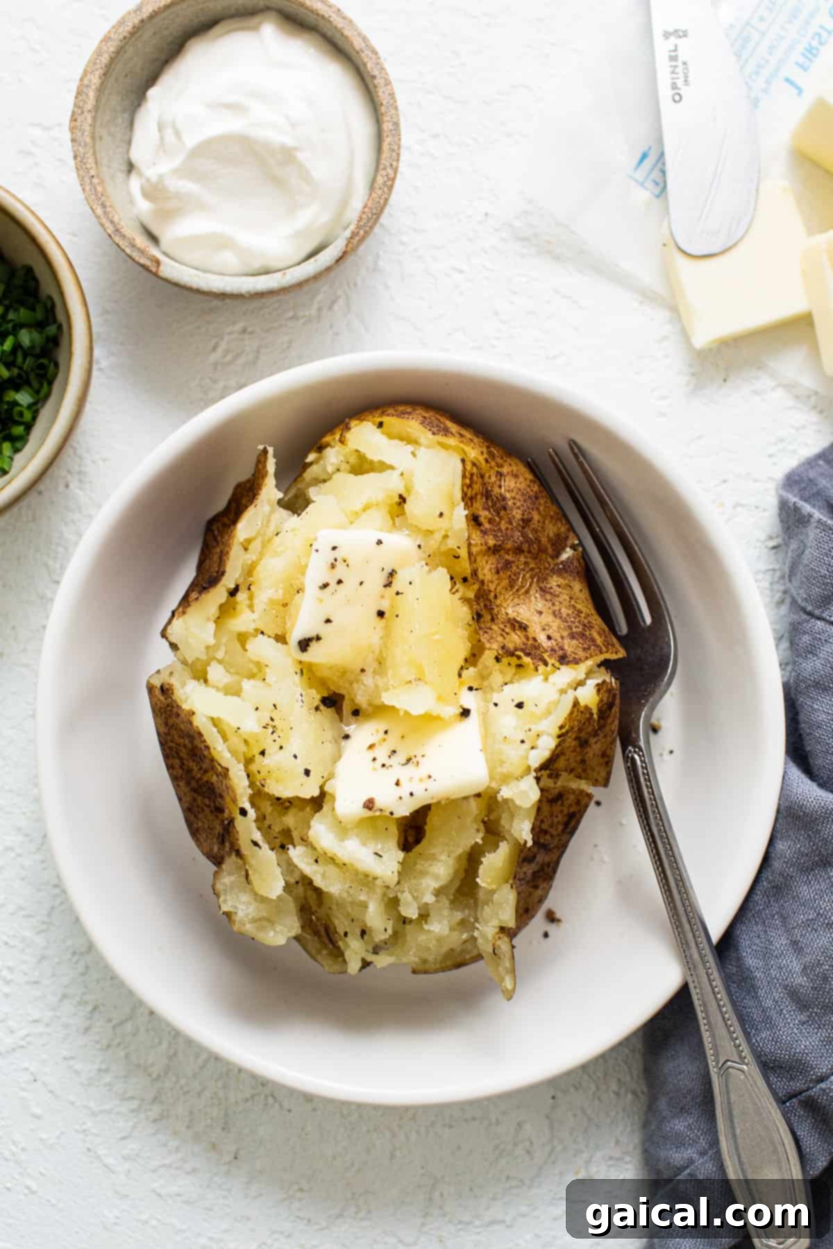 A freshly baked potato in a bowl, topped with a pat of butter.