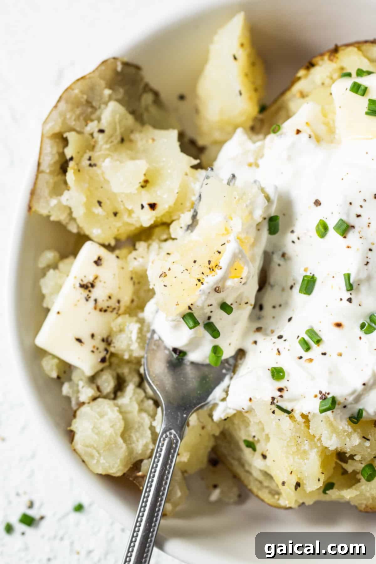 A fluffed baked potato with a fork, showing its soft interior.