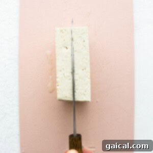 A person cutting a piece of tofu on a pink surface.