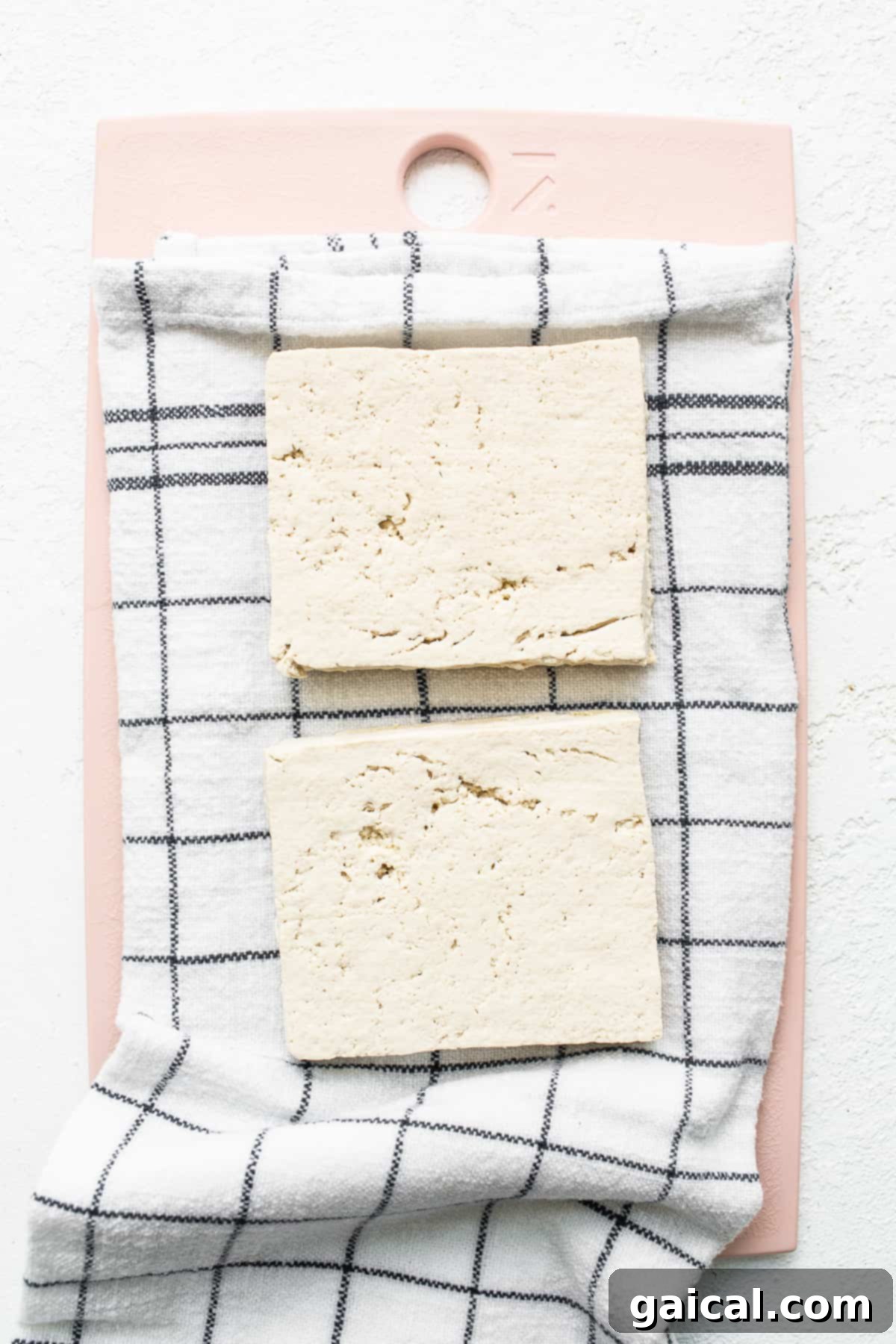 A block of firm tofu, freshly sliced into uniform cubes on a pink cutting board, ready for the next step.
