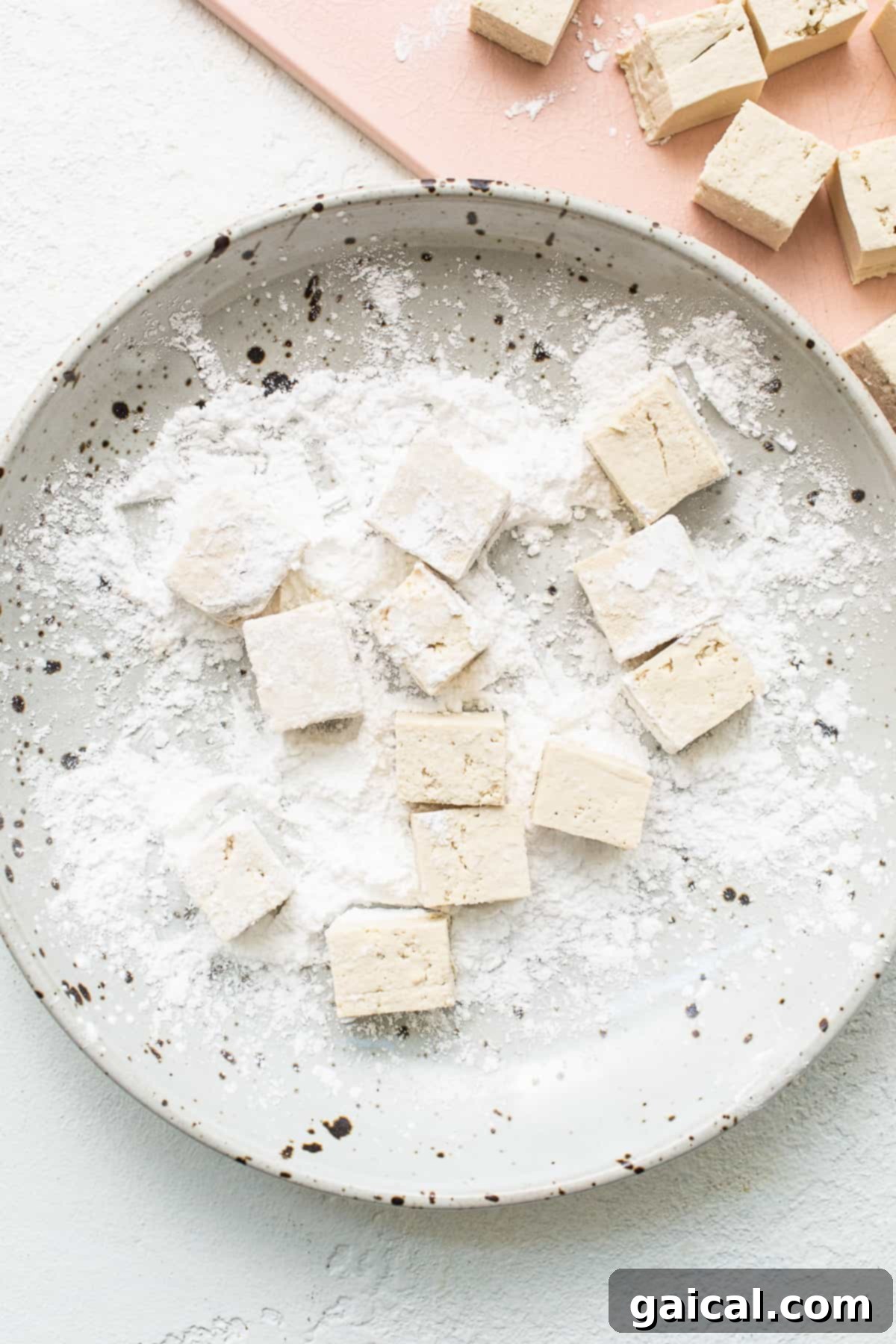Tofu cubes being gently tossed in cornstarch and seasoning in a bowl, ensuring an even coating for maximum crispiness.