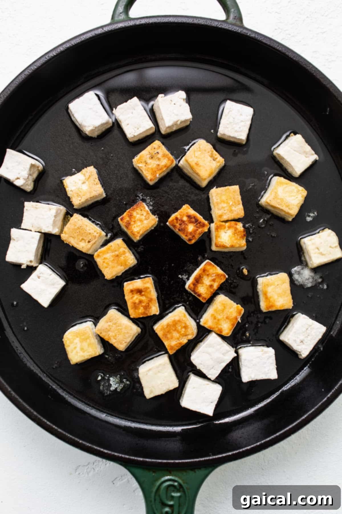 Crispy tofu cubes sizzling and browning in hot oil in a skillet, showcasing the pan-frying process.