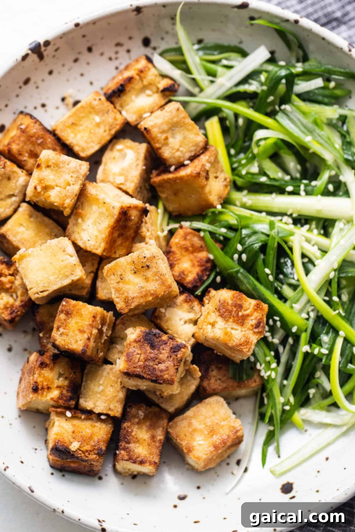 A plate of perfectly golden and crispy pan-fried tofu, garnished and ready to be enjoyed as a delicious plant-based meal.
