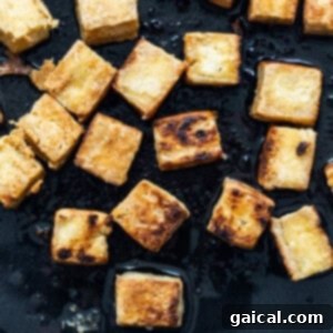 Crispy tofu cubes being pan-fried in a skillet, showcasing the golden-brown exterior.